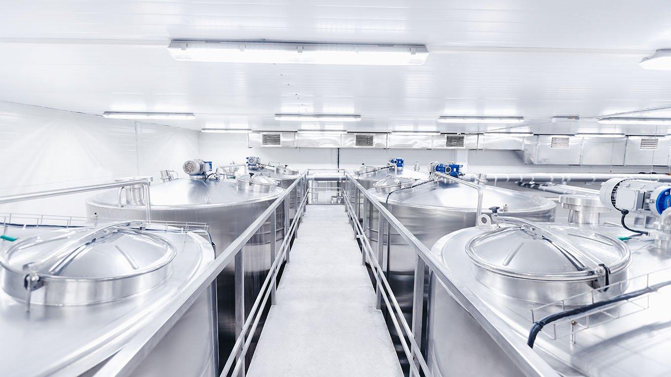 Industrial facility with large stainless steel tanks used for processing or storage, with central walkway and overhead lighting.